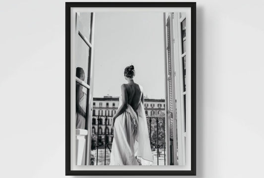 Framed black and white photograph of a woman in a dress looking out a window.