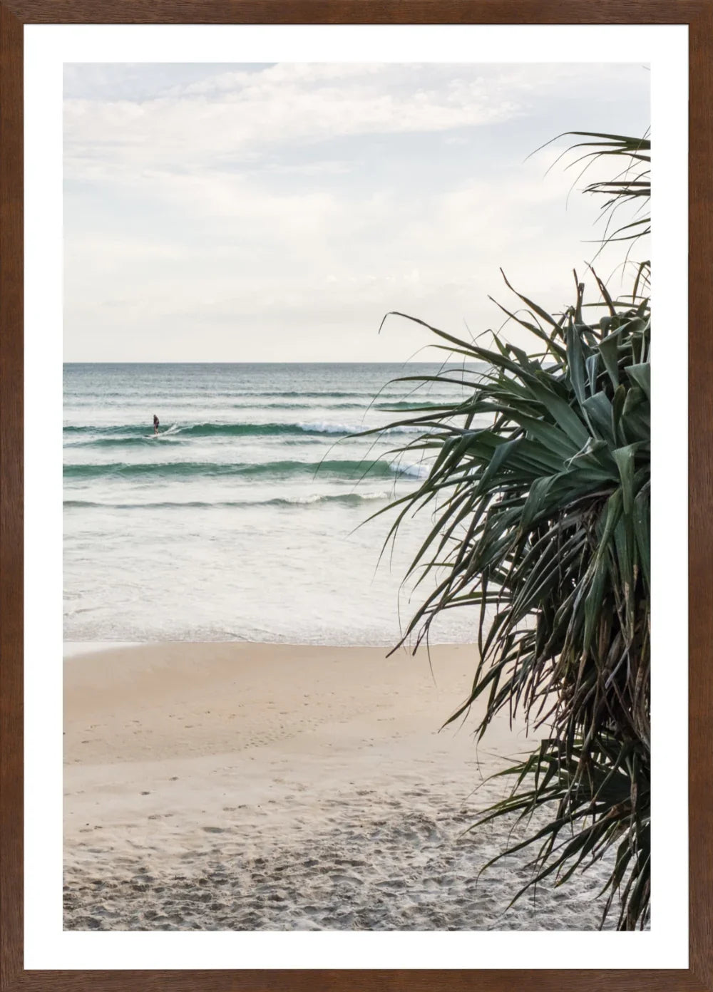 Wategos Beach scene with waves and a surfer, framed by tropical plants.
