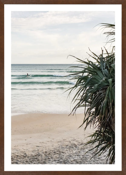 Wategos Beach scene with waves and a surfer, framed by tropical plants.