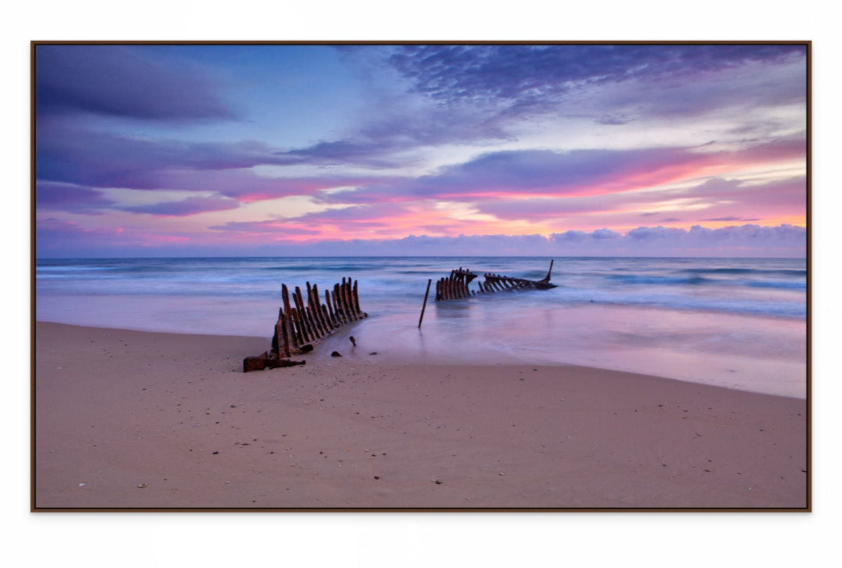 Framed dark wood pring of wreck on a dicky beach with a colorful sunset sky