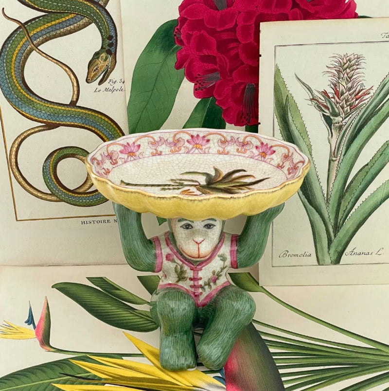 Decorative porcelain monkey figurine holding a bowl with pink floral pattern and palm tree motive