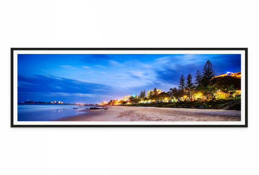 Framed panoramic view of mooloolaba beach at night with lights and trees.
