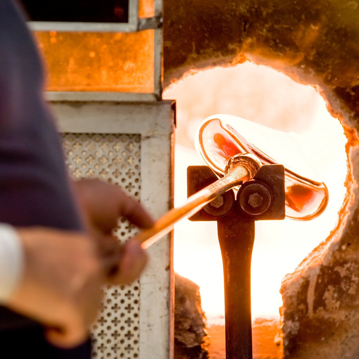 Glassblowing process with a glass artist using a blowtorch inside a furnace.