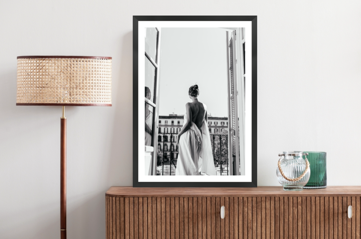 Framed black and white artwork of a woman in a dress, looking out a window in Paris.